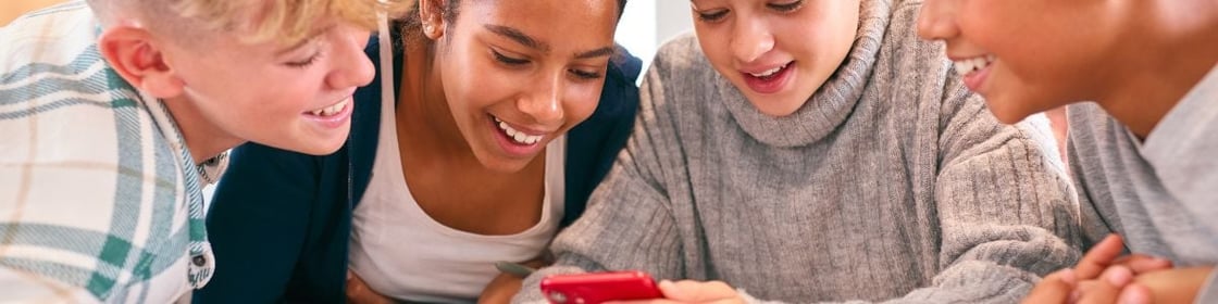 Four smiling young people looking at a phone